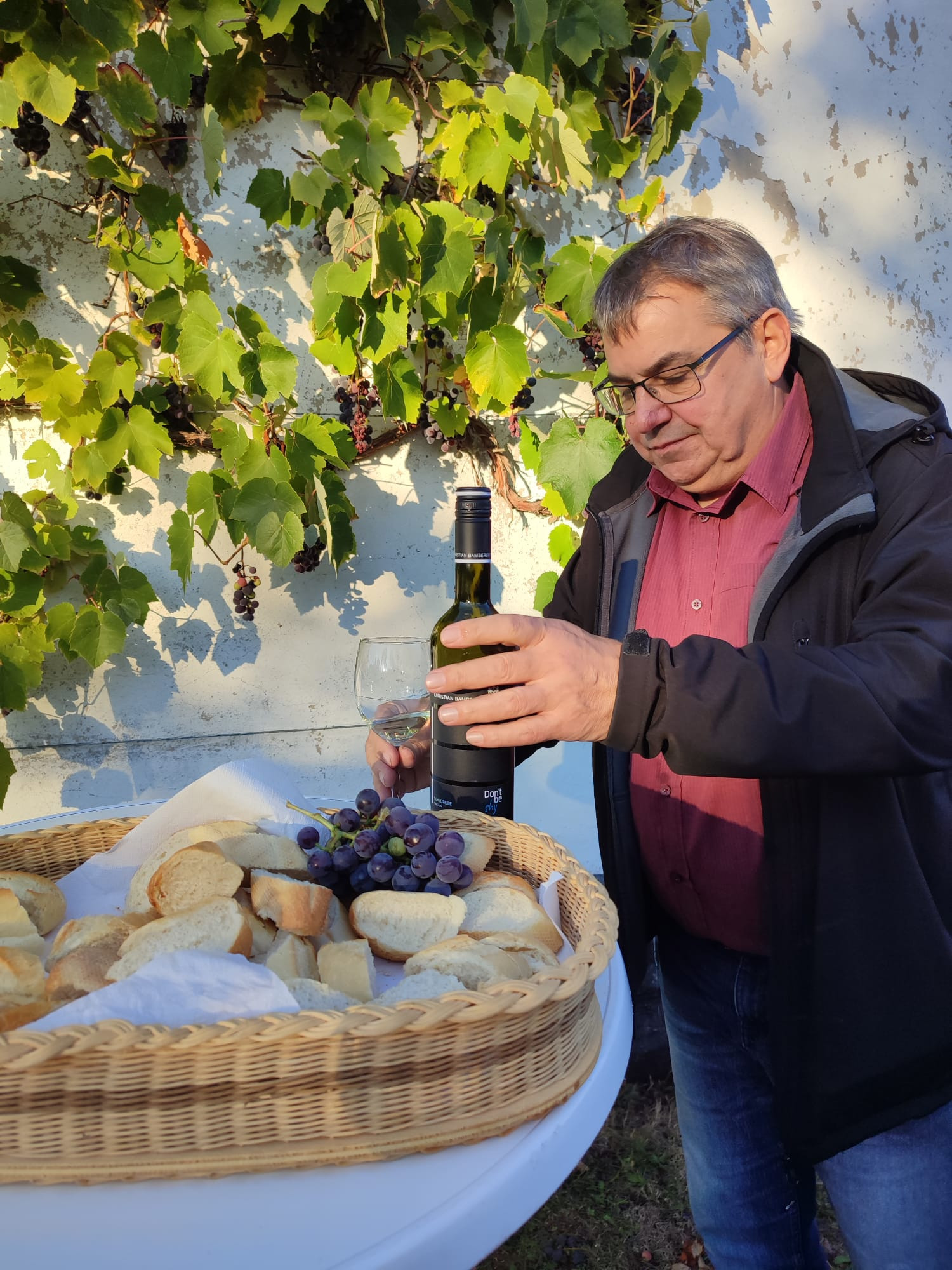 Detlev Schaub mit Wein und Brot vor einer Rebe