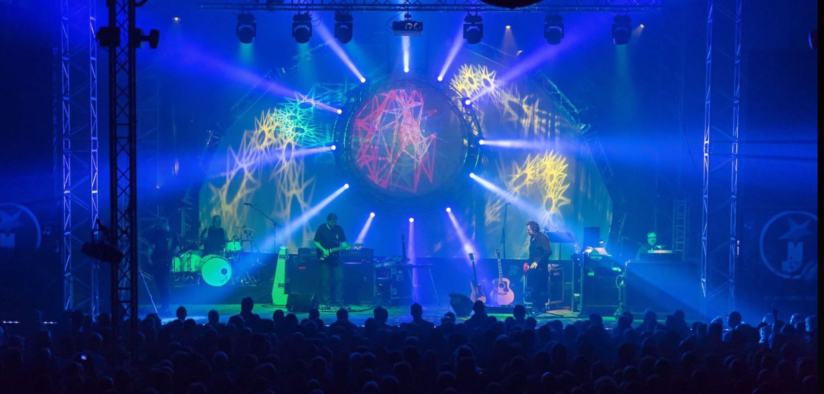 Eine Band steht auf der Bühne in blauem Scheinwerferlicht.