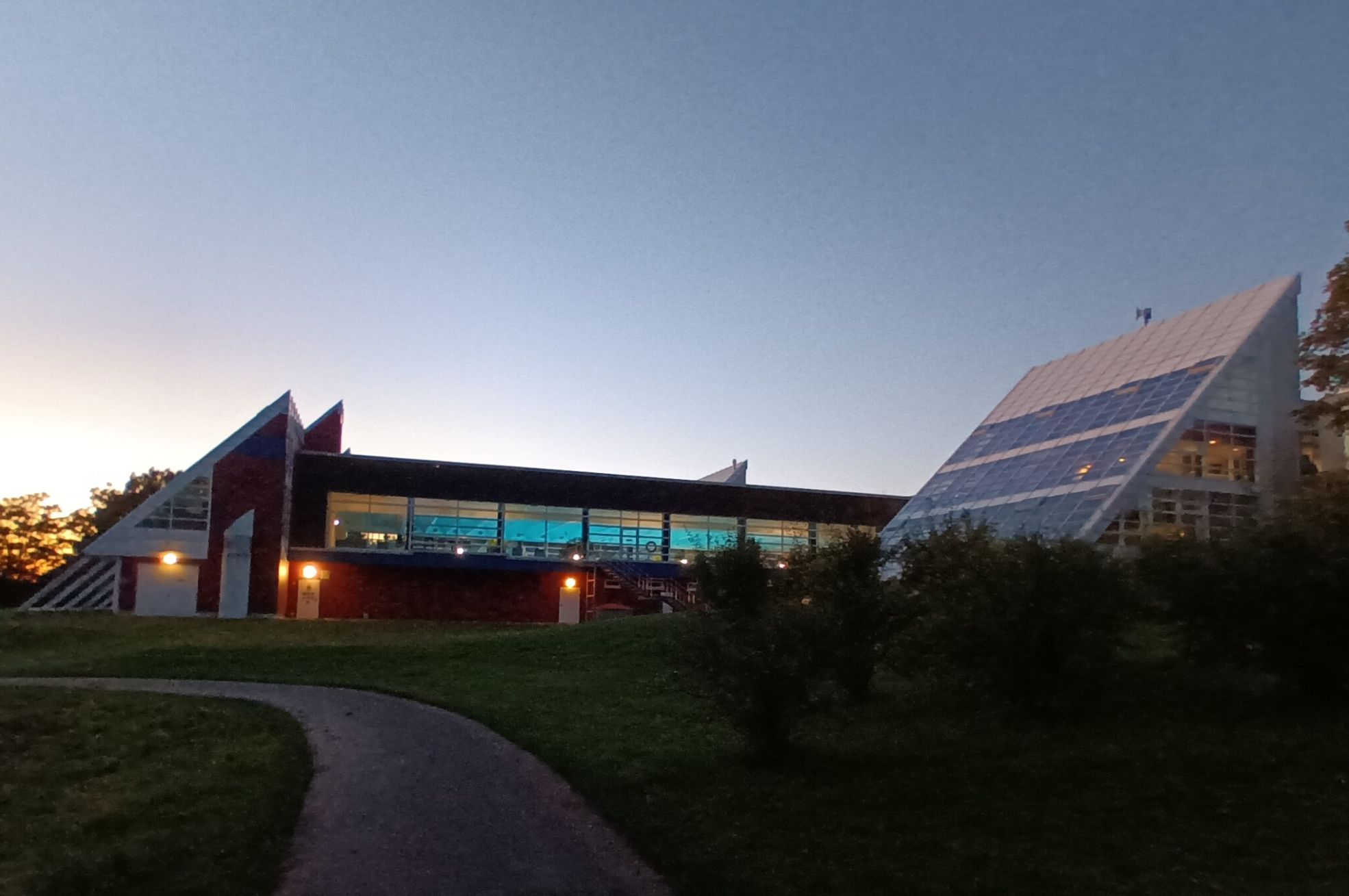 Thermalsolbad mit beleuchtetem Innenbecken vor blauem Abendhimmel und grüner Wiese.