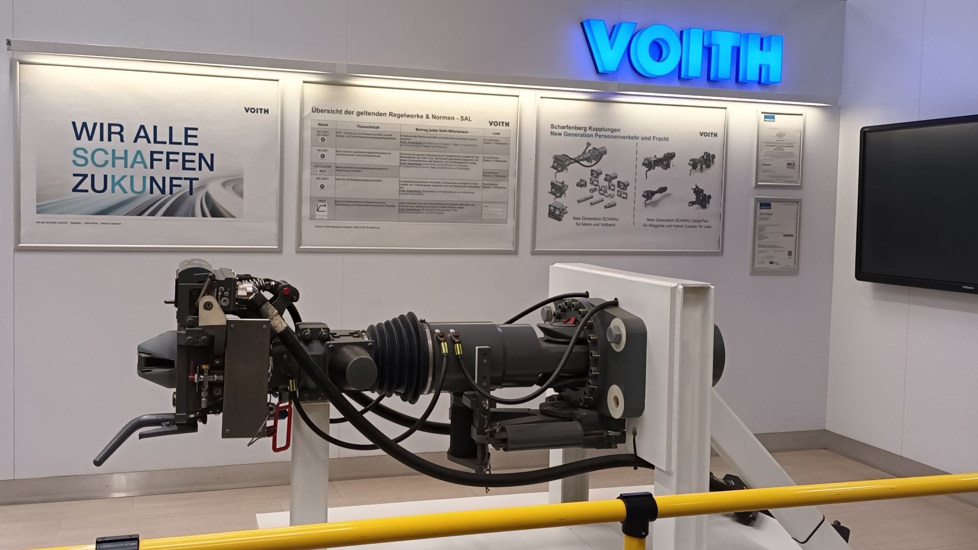 Ausstellungsraum bei Voith mit beleuchtetem Firmenlogo und Exponat einer modernen Zugkupplung.
