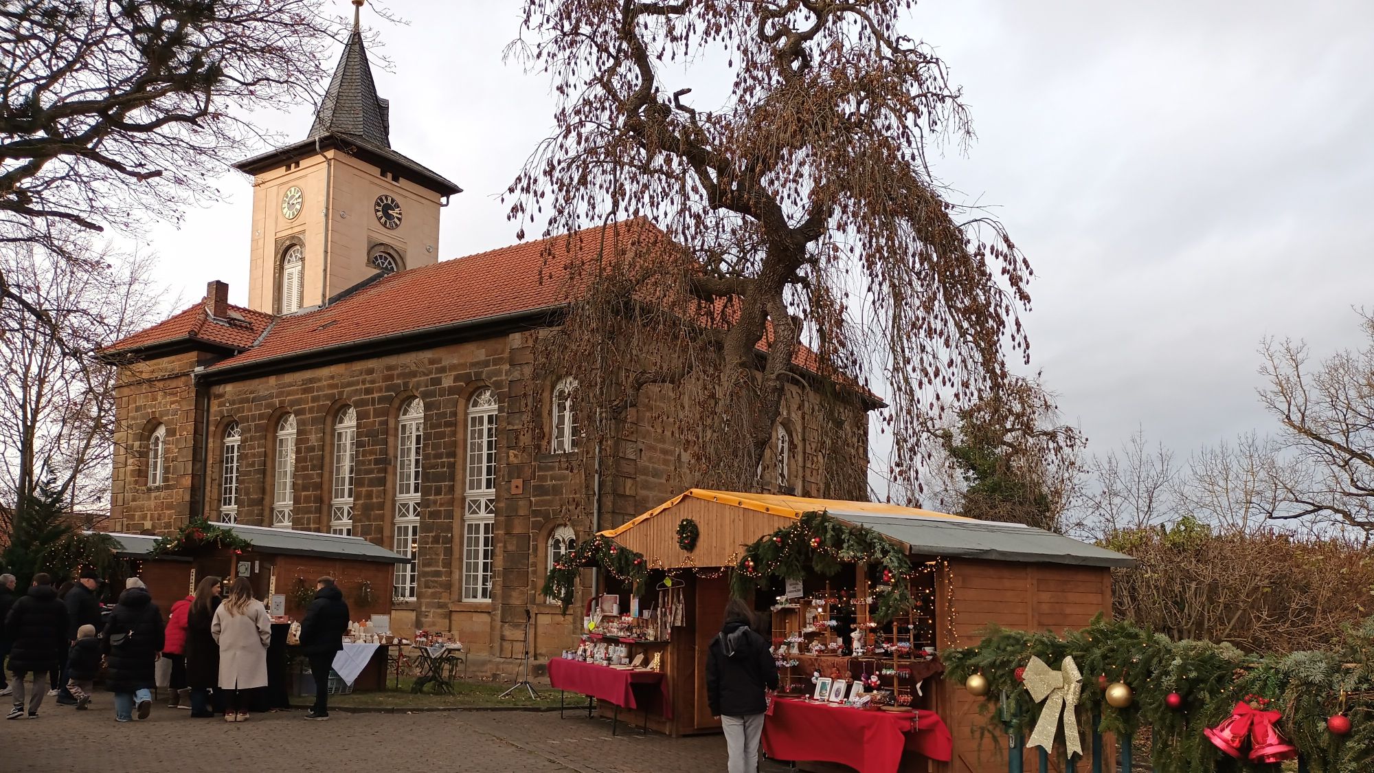Weihnachtsmarktbuden vor historischer Kirche in Salzgitter-Gitter mit Besuchern.