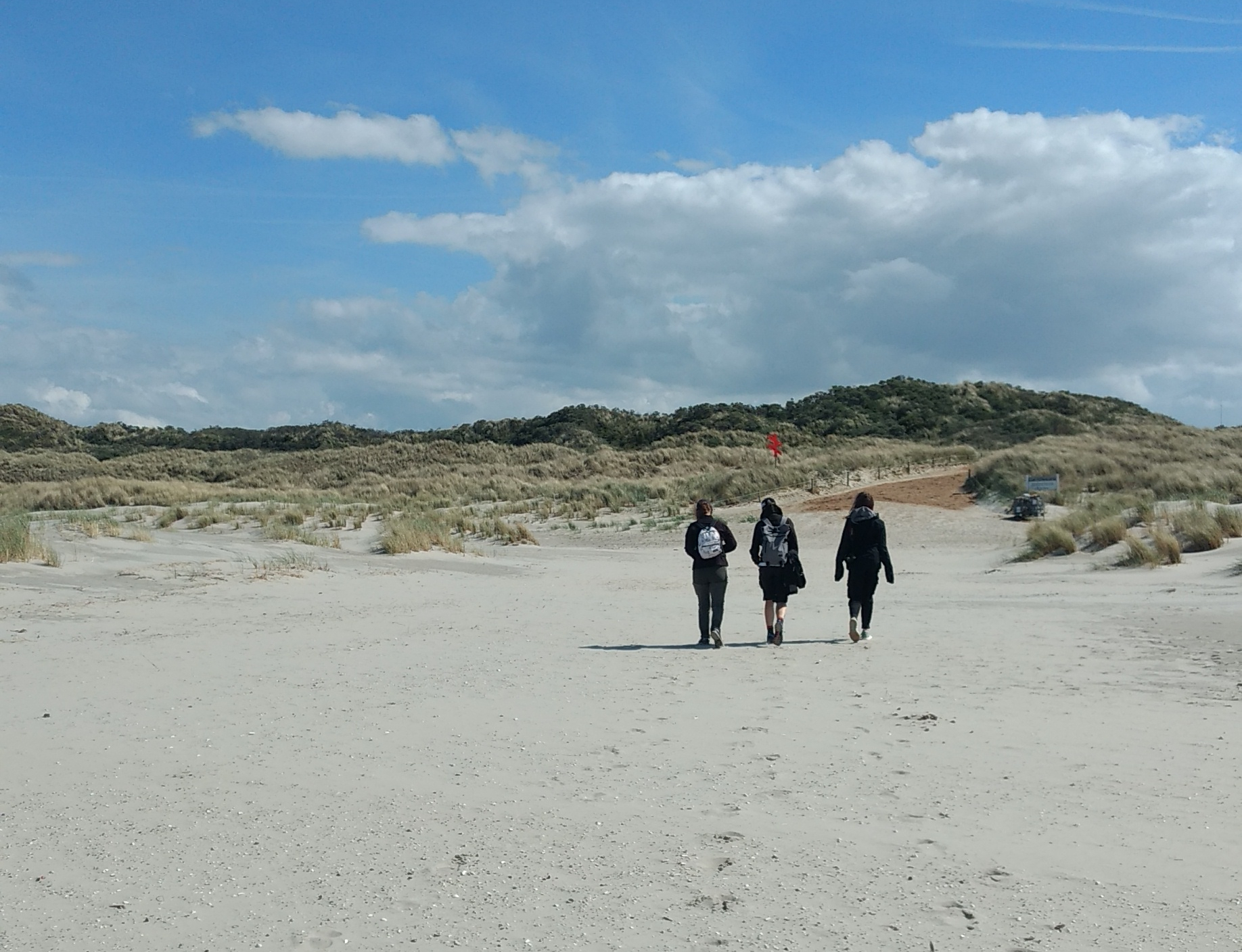 Das Foto zeigt die Dünen und drei Spaziergänger.