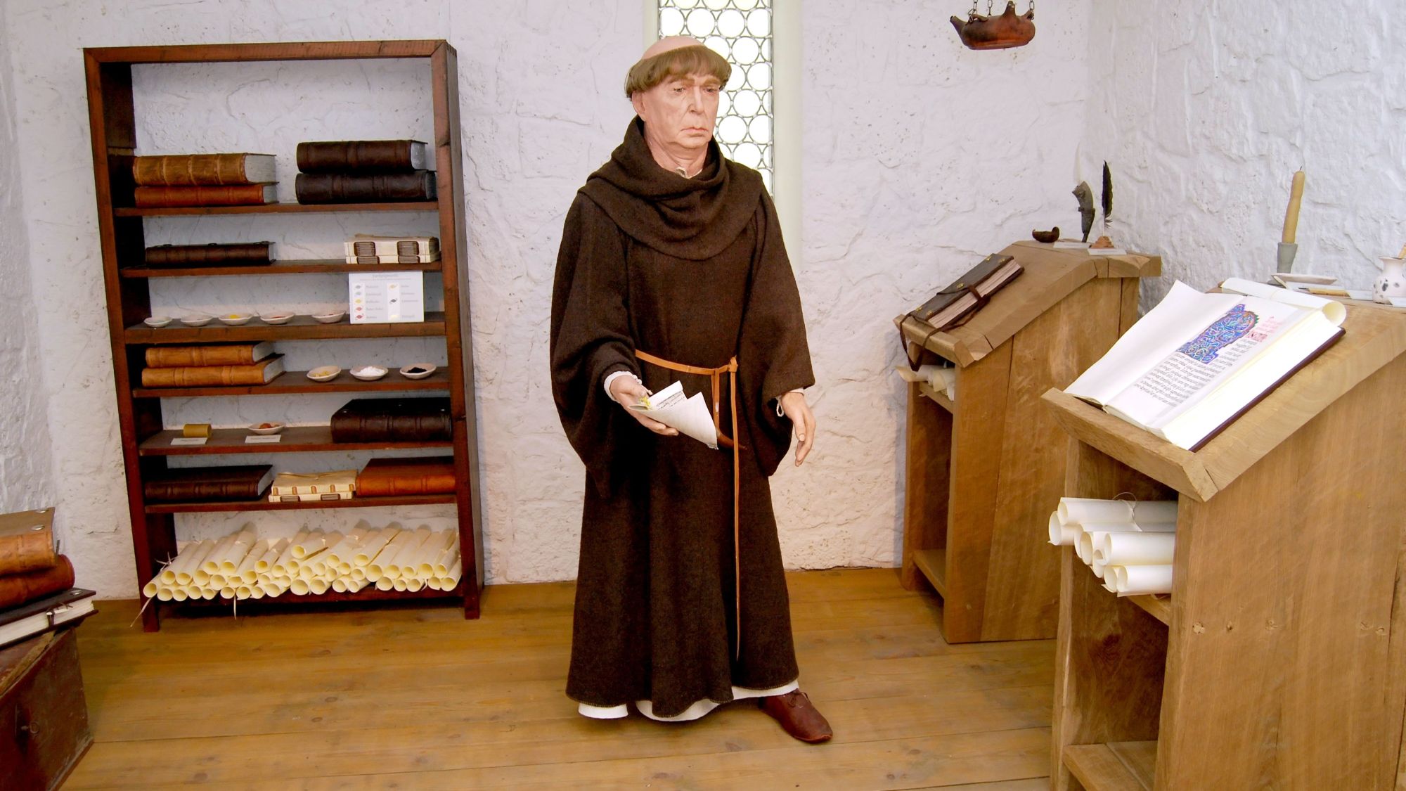 Figur eines Mönchs in Kutte in einer historischen Schreibstube mit Büchern und Pulten.